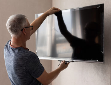 Side view of mature technician installing tv at home.